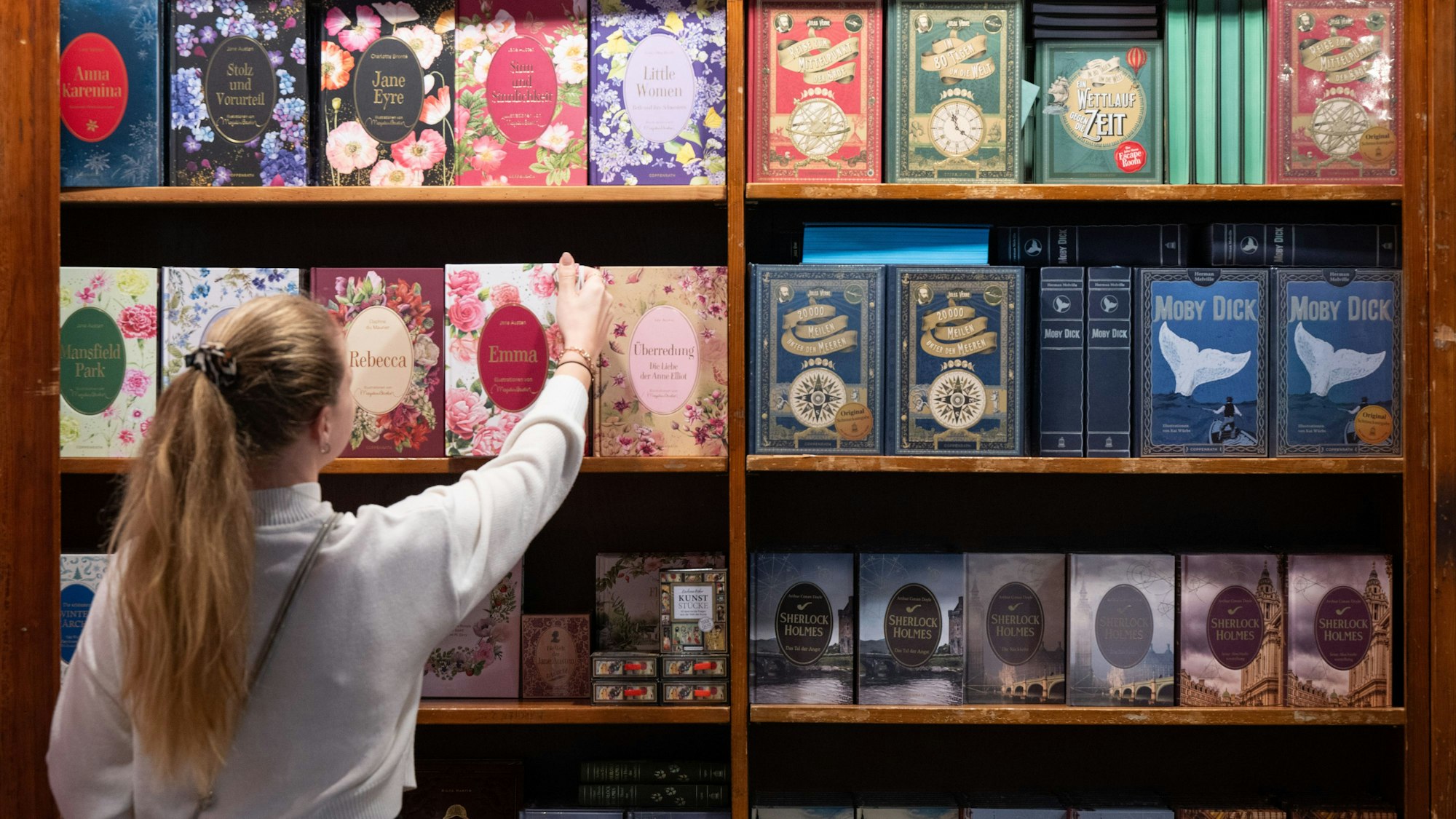 Eine Frau nimmt ein Buch aus einem Regal am Messsestand des Verlags Coppenrath.