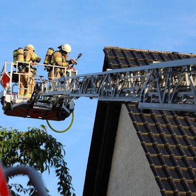 Feuerwehrleute inspizieren vom Korb einer Drehleiter aus ein Hausdach.