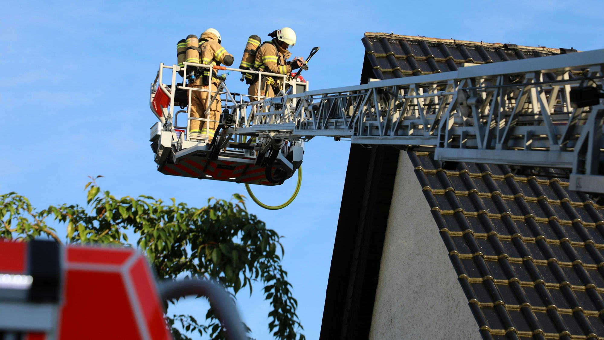 Feuerwehrleute inspizieren vom Korb einer Drehleiter aus ein Hausdach.