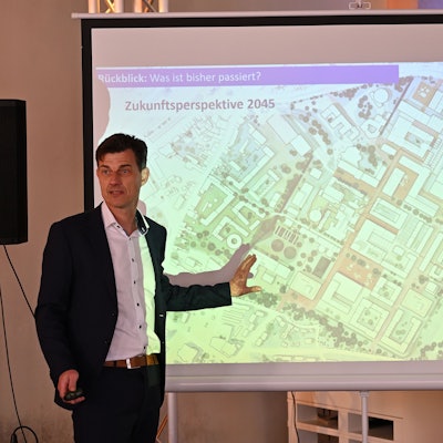 Oliver Brügge steht vor einer Leinwand ., wo ein Plan vom Zanders-Gelände abgebildet ist.