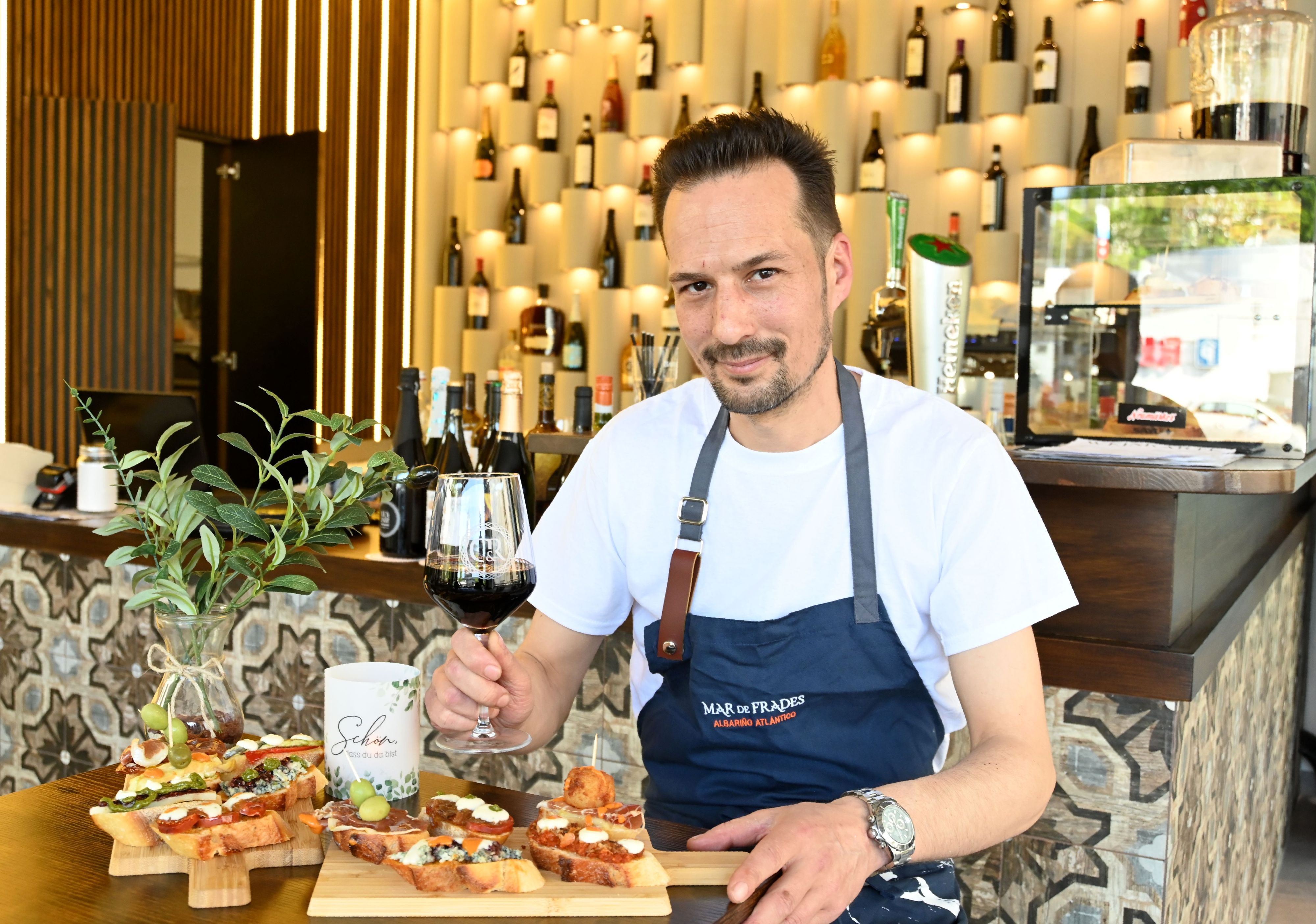 Ein Mann mit Wein in der Hand schaut in die Kamera.