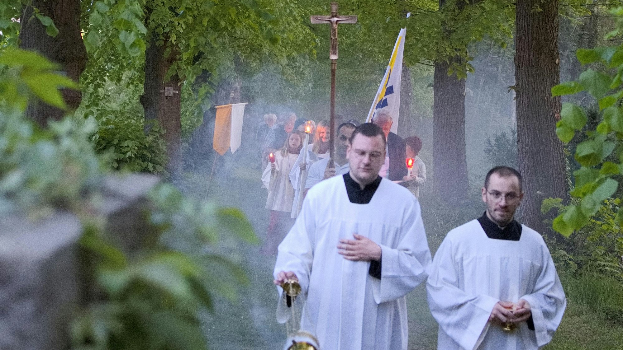 Zwei Messdiener ziehen vor einem Prozessionszug durch einen Wald.