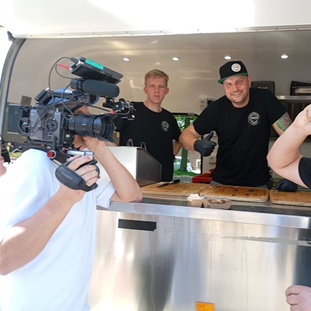 Das Foto zeigt einen Kameramann bei der Arbeit vor einem Imbisswagen.