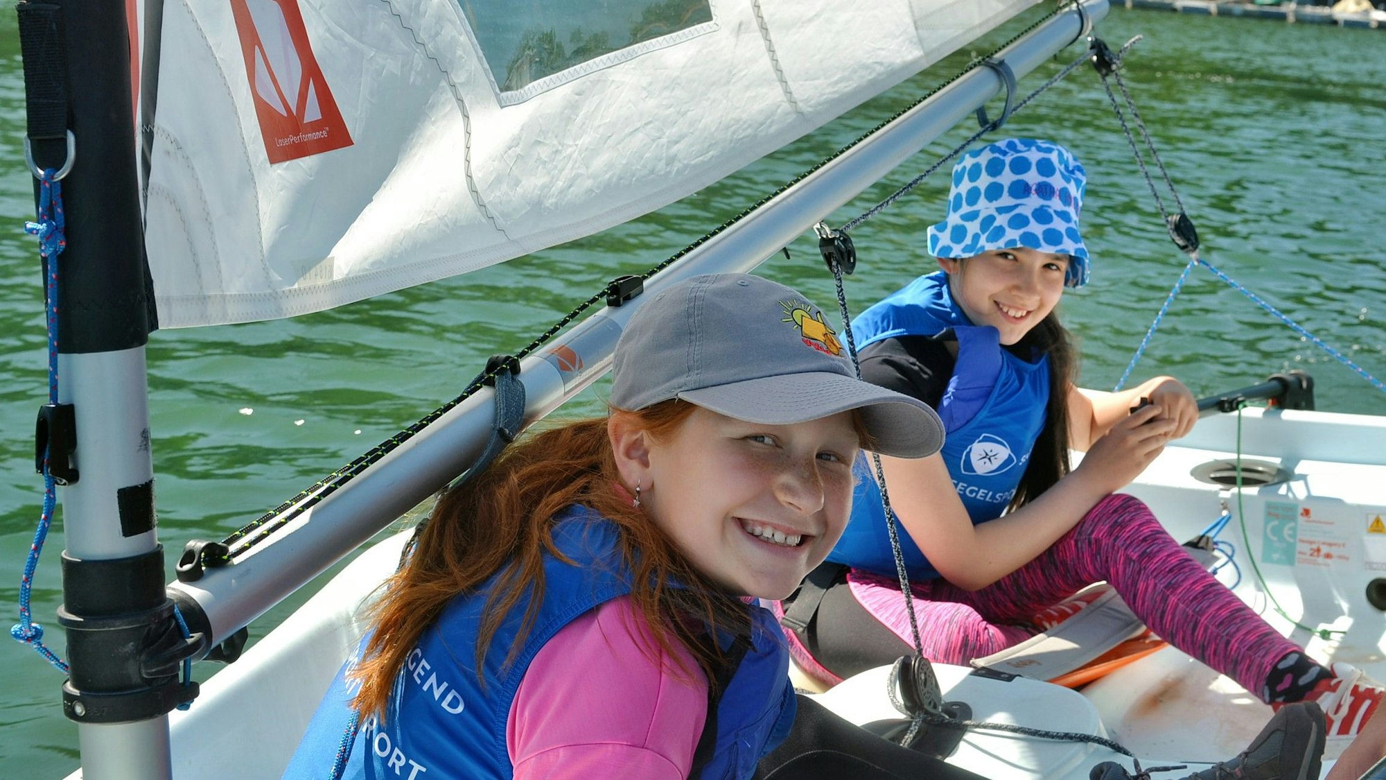 Die beiden Kinder sitzen in einem Segelboot und lächeln.