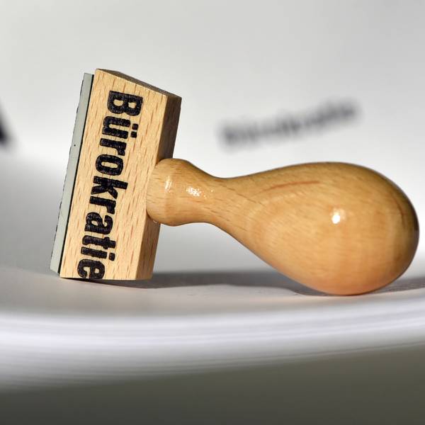Ein Stempel mit der Aufschrift „Bürokratie“ liegt auf Papieren.
