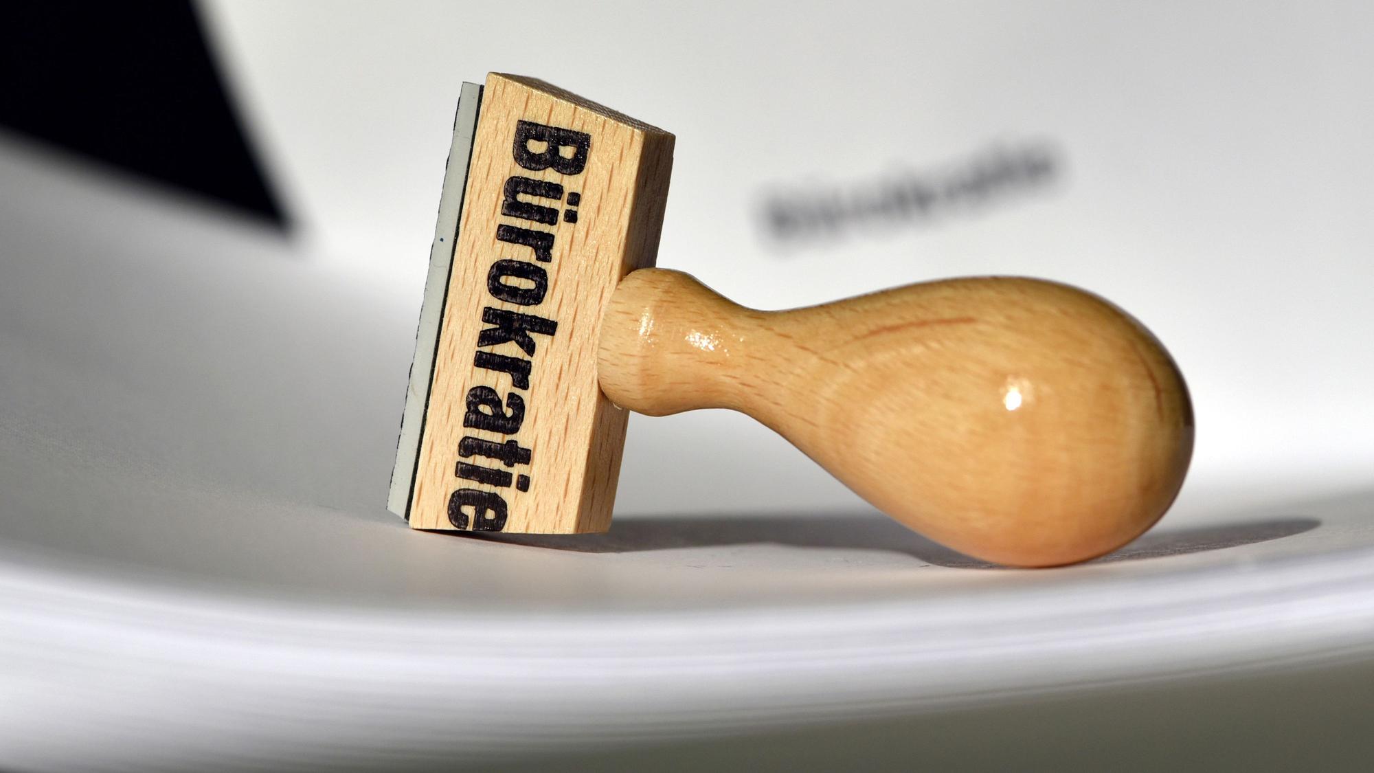 Ein Stempel mit der Aufschrift „Bürokratie“ liegt auf Papieren.
