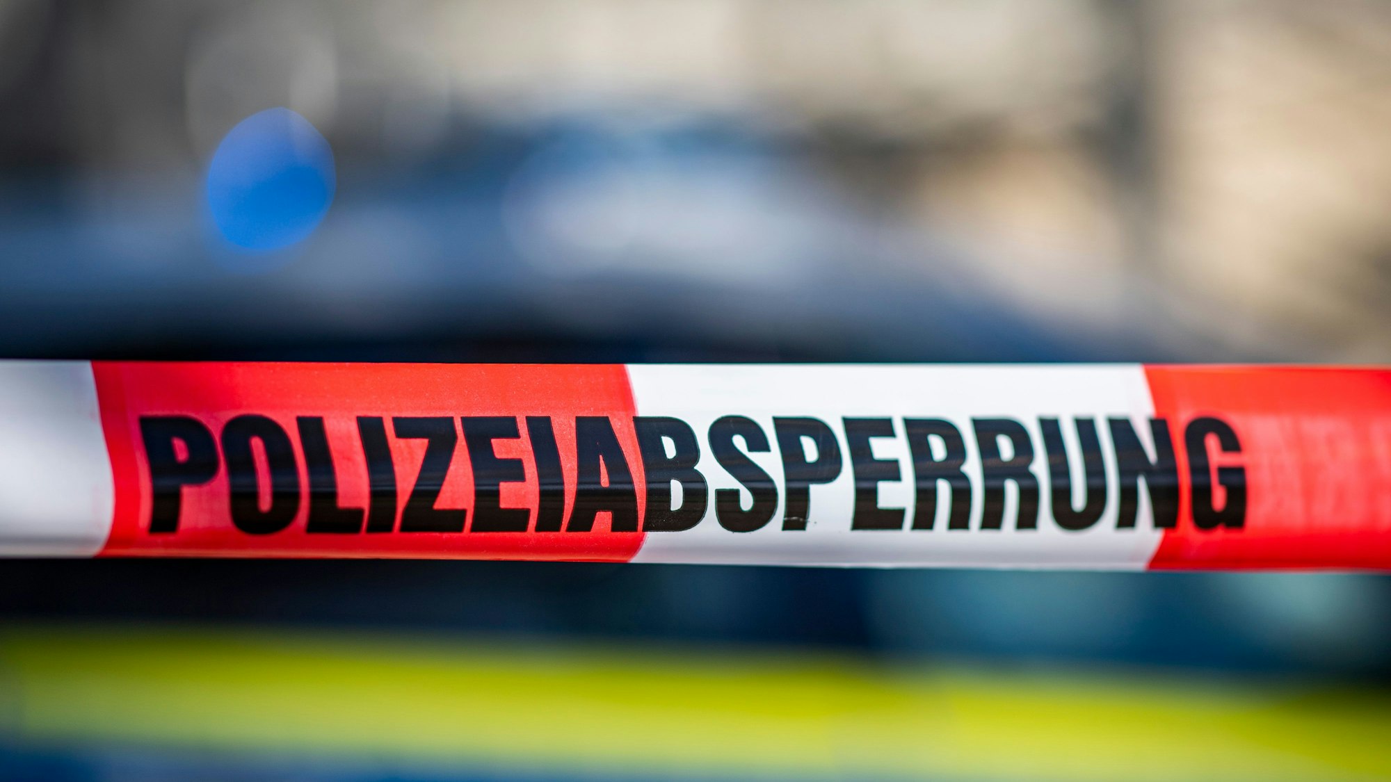 Ein Absperrband mit der Aufschrift „Polizeiabsperrung“ ist vor einem Polizeiwagen aufgespannt.