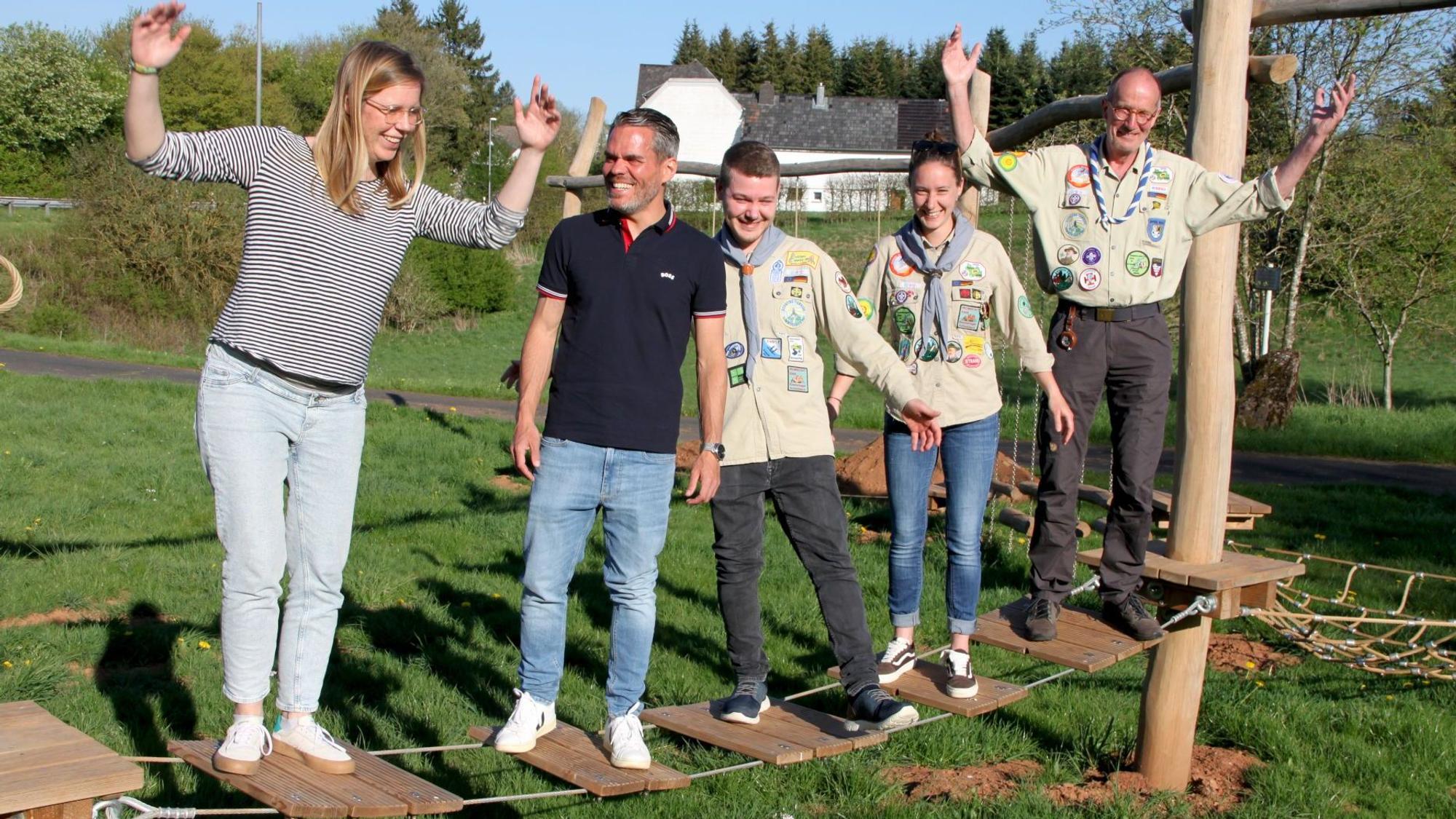 Fünf Personen, darunter drei in Pfadfinderuniformen, stehen auf einem wackeligen Teil des neuen Niedrigseilparcours.