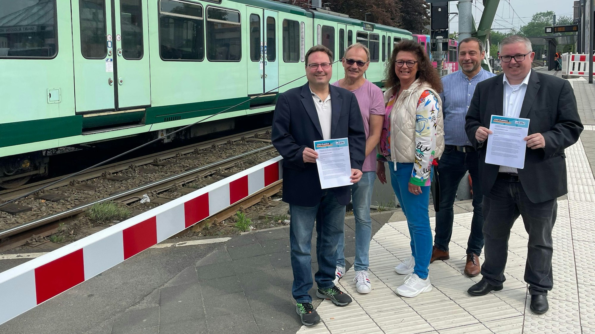 Mitglieder der CDU-Ratsfraktion stehen an der Trasse der Stadtbahnlinie 66 und zeigen ihr Positionspapier zu den geplanten Änderungen auf der Linie.