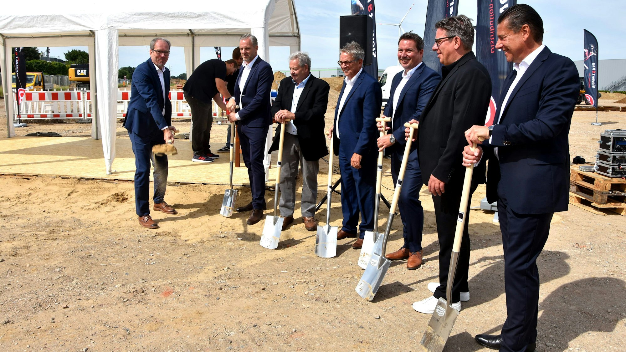 Das Bild zeigt Männer mit Anzügen, die Spaten in der Hand halten.