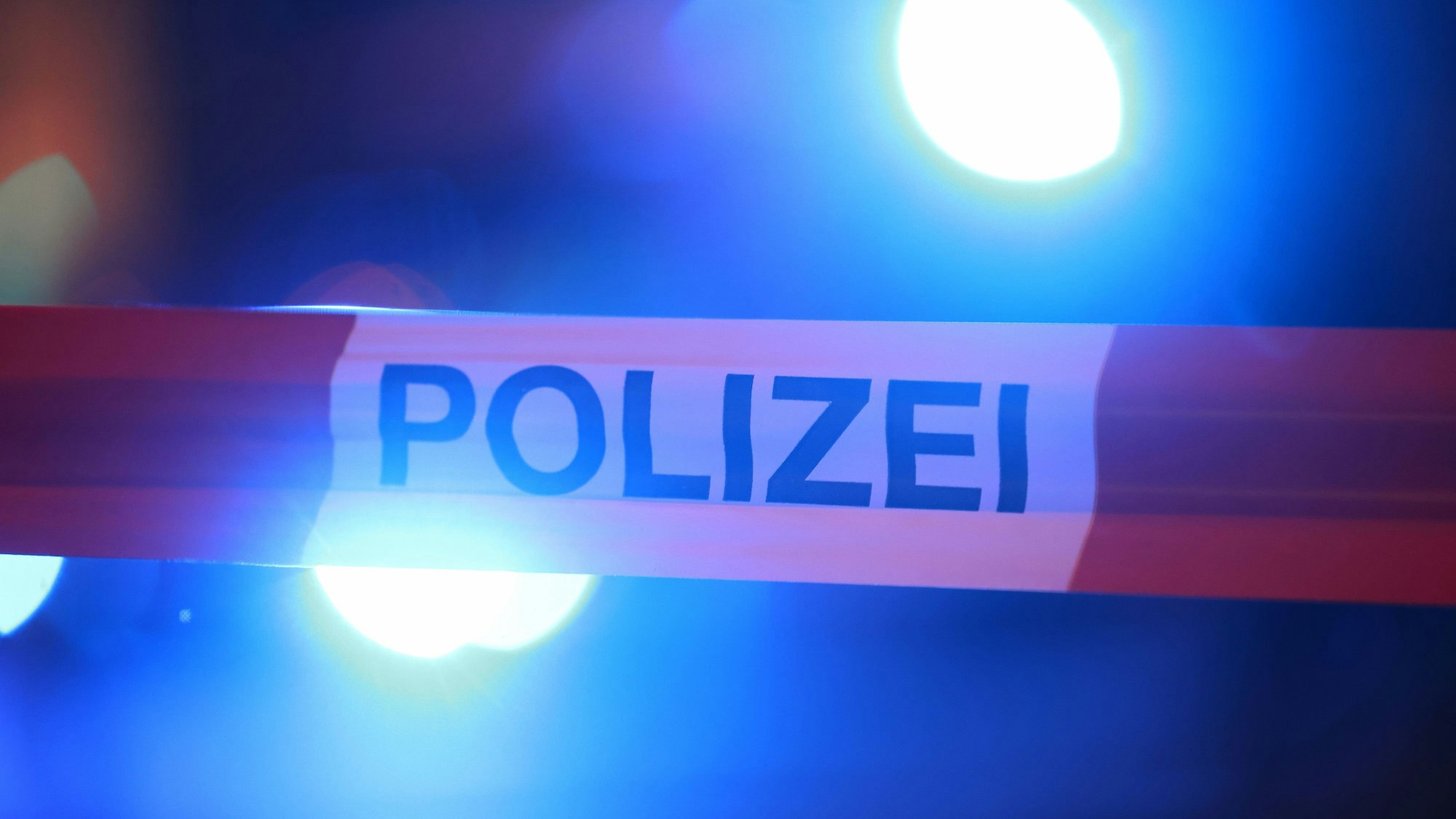 Blaulichter leuchten hinter einem Absperrband der Polizei.