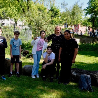 Zwei Jungs, drei Mädchen und eine Frau mit langem blondem Haar stehen in einem Garten.