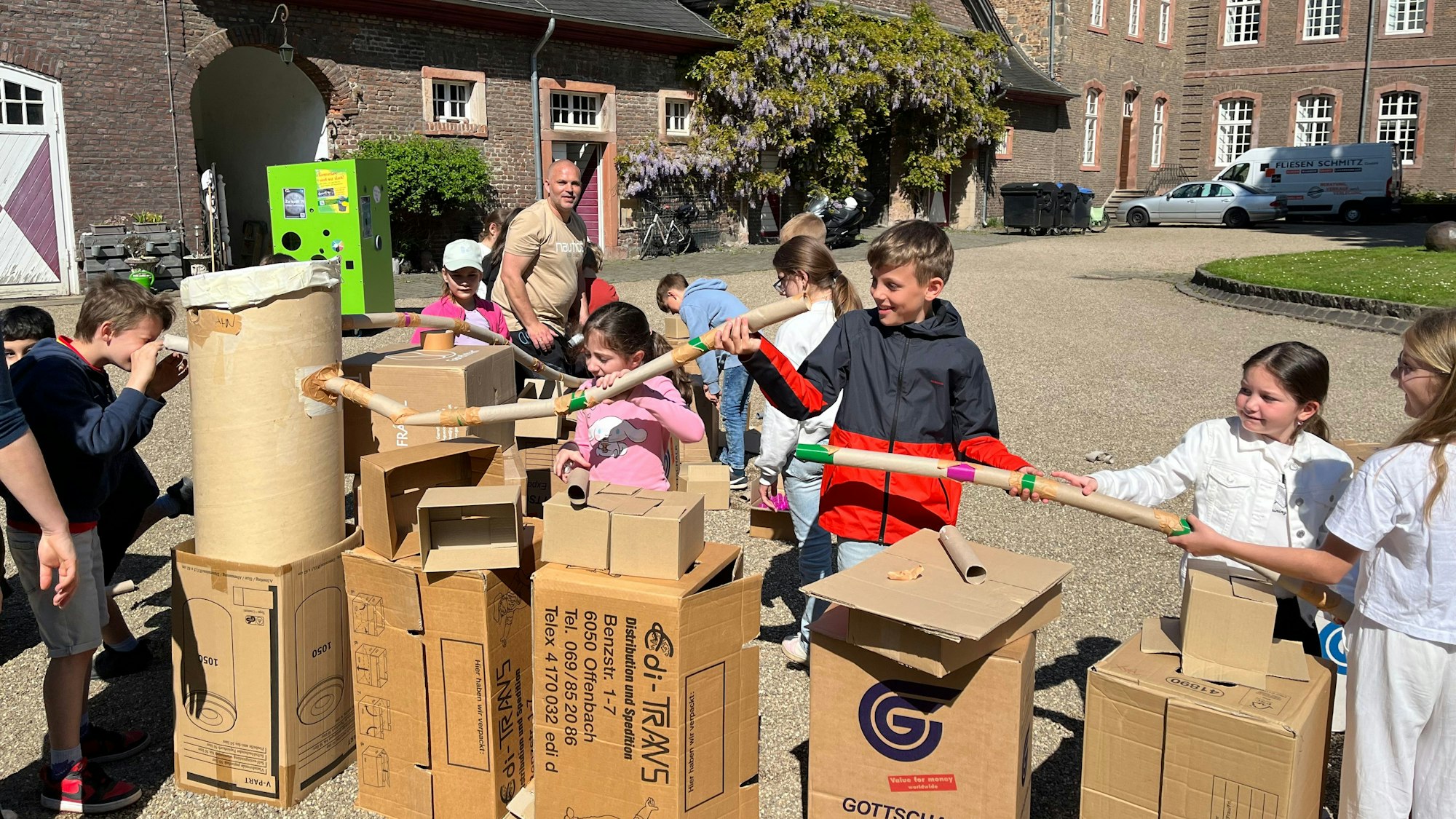 Im Hof des Wahner Schlosses bauen Kinder aus Haushalts-Materialien und Verbindungselementen aus dem 3D-Drucker eine große Murmelbahn.