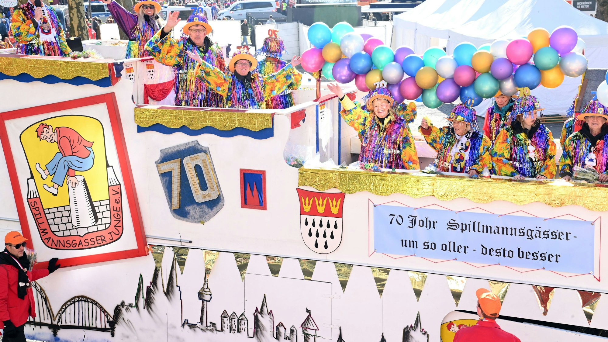 Ein Karnevalswagen, geschmückt mit Luftballons und bunt gekleideten Frauen, die darauf fahren, ist zu sehen.