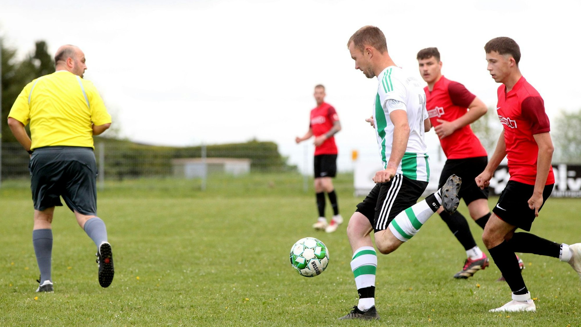 Marcel Hupp wird von zwei Hellenthalern verfolgt. Der Schiedsrichter steht mit dem Rücken zum Geschehen.