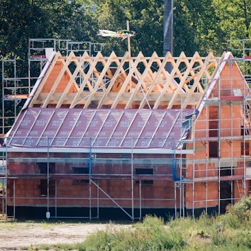 Ein Richtkranz weht am Dachstuhl eines neu gebauten Einfamilienhauses in einer Neubausiedlung.