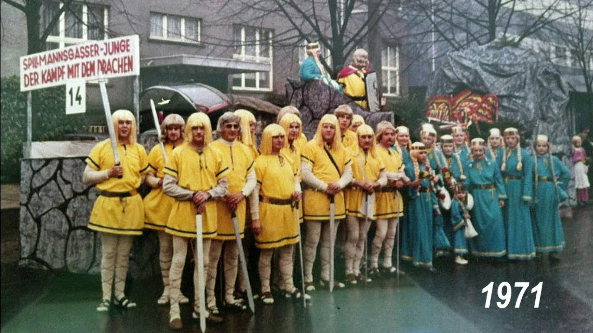 Männer in gelben Kostümen und Perücken sowie Kinder in Burgfräulein-Kostümen stehen auf der Straße.