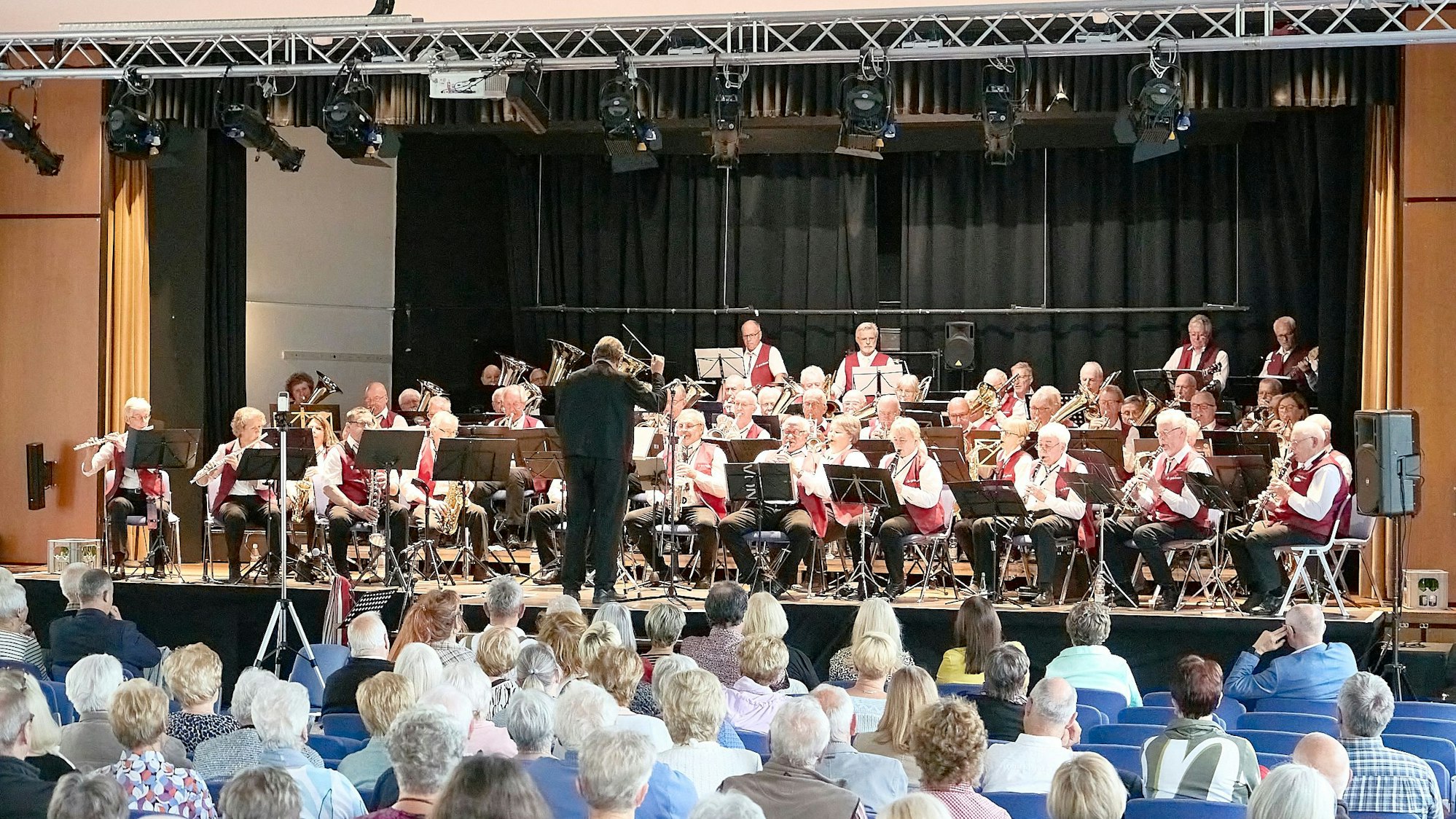 In der Aula sitzen viele Gäste, auf der Bühne sitzt das Ü-50 Blasorchester mit seinen 60 Mitgliedern.
