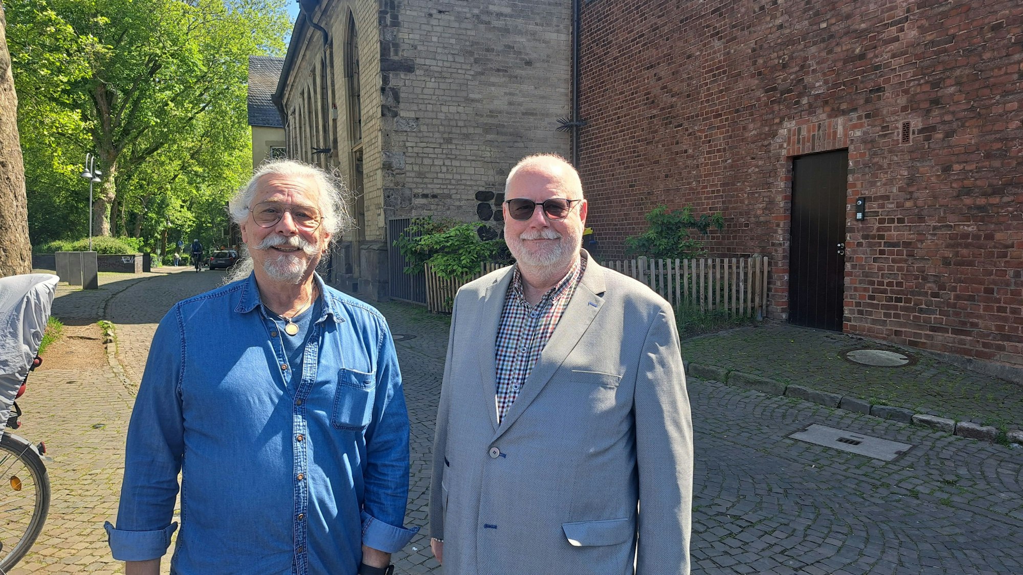 Zwei Männer stehen vor einem Backstein-Gebäude.