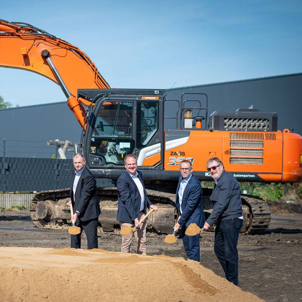 Das Foto zeigt vier Männer mit Spaten vor einem Sandhaufen, im Hintergrund ein Bagger.