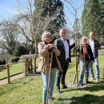 Zwei Frauen und zwei Männer stehen in Nettersheim auf einer Wiese an frisch gepflanzten Bäumen.