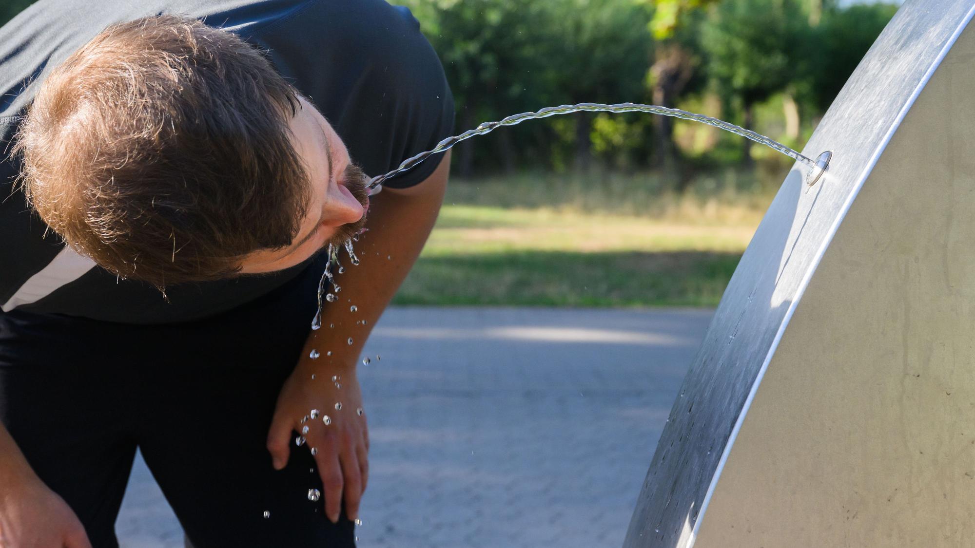 Ein Sportler trinkt Wasser an einem öffentlichen Trinkwasserspender.