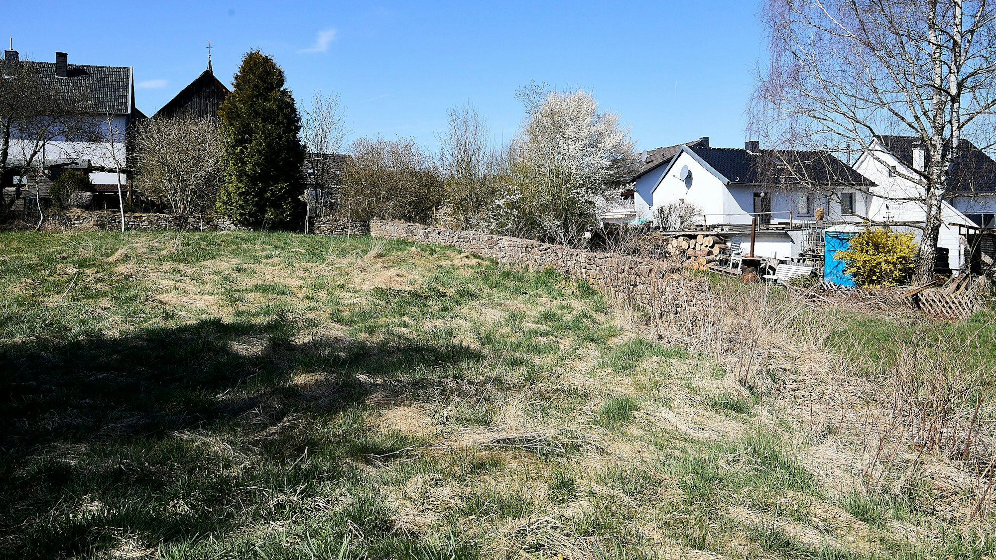 Die Wiese ist der ehemalige Friedhof von Nettersheim. Im Hintergrund sind einige Häuser des Ortes zu sehen.