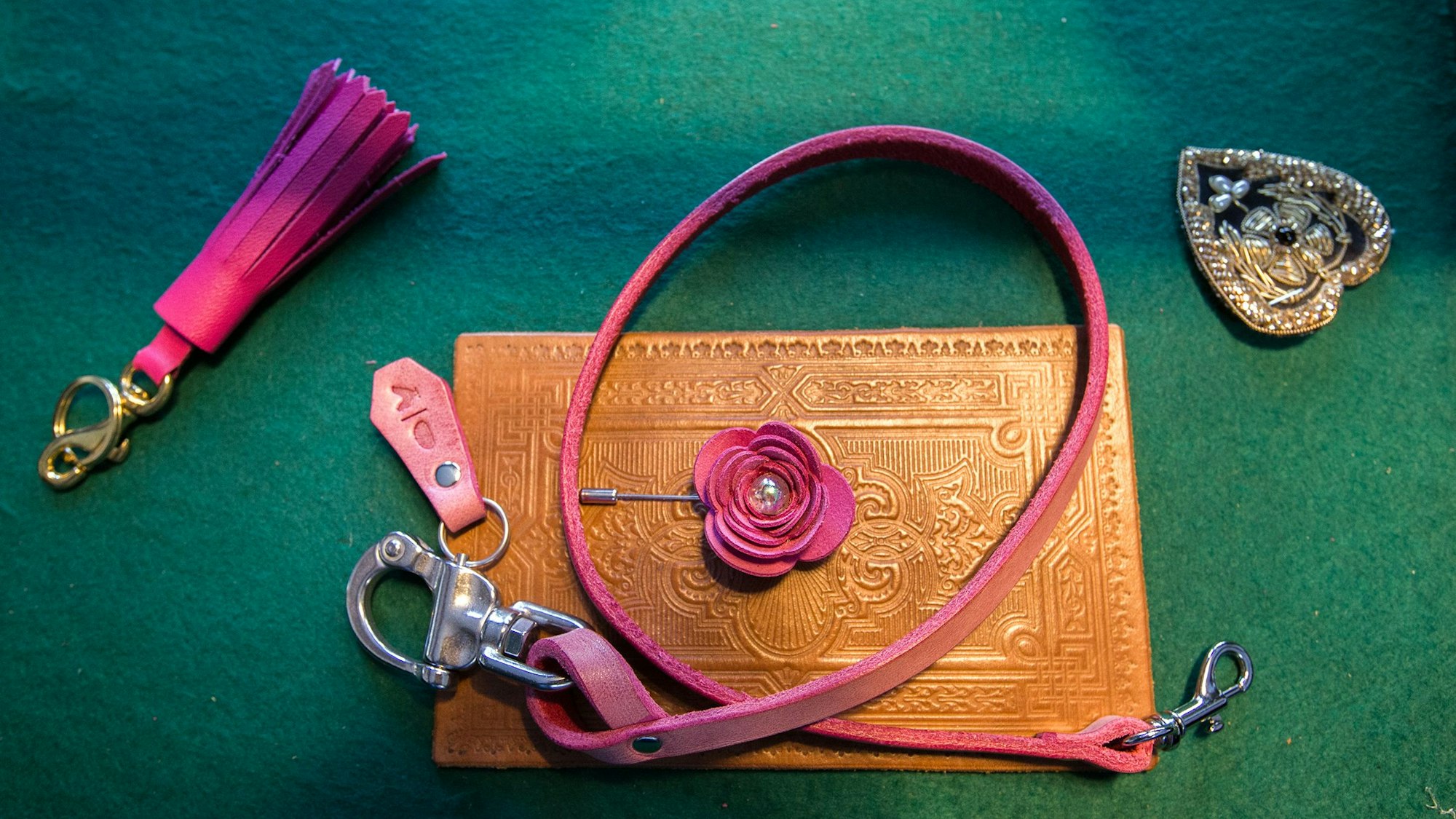 Auf einer grünen Filzunterlage liegen verschiedene Gegenstände aus Leder, wie etwa eine rosa Hundeleine oder ein Schlüsselanhänger mit pinken Fransen.