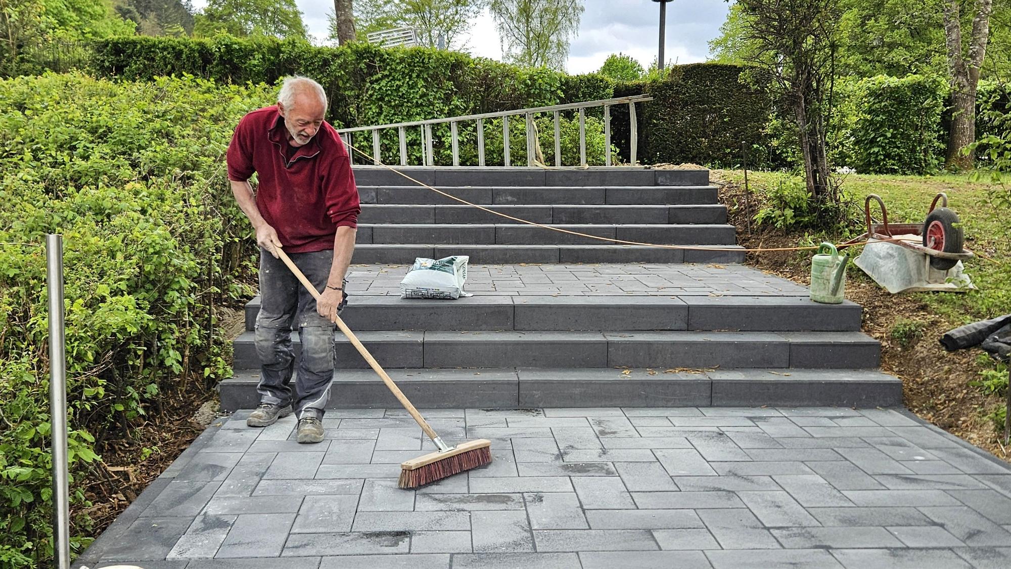 Ein Arbeiter verteilt den Fugensand zwischen den Platten der neuen Treppe.