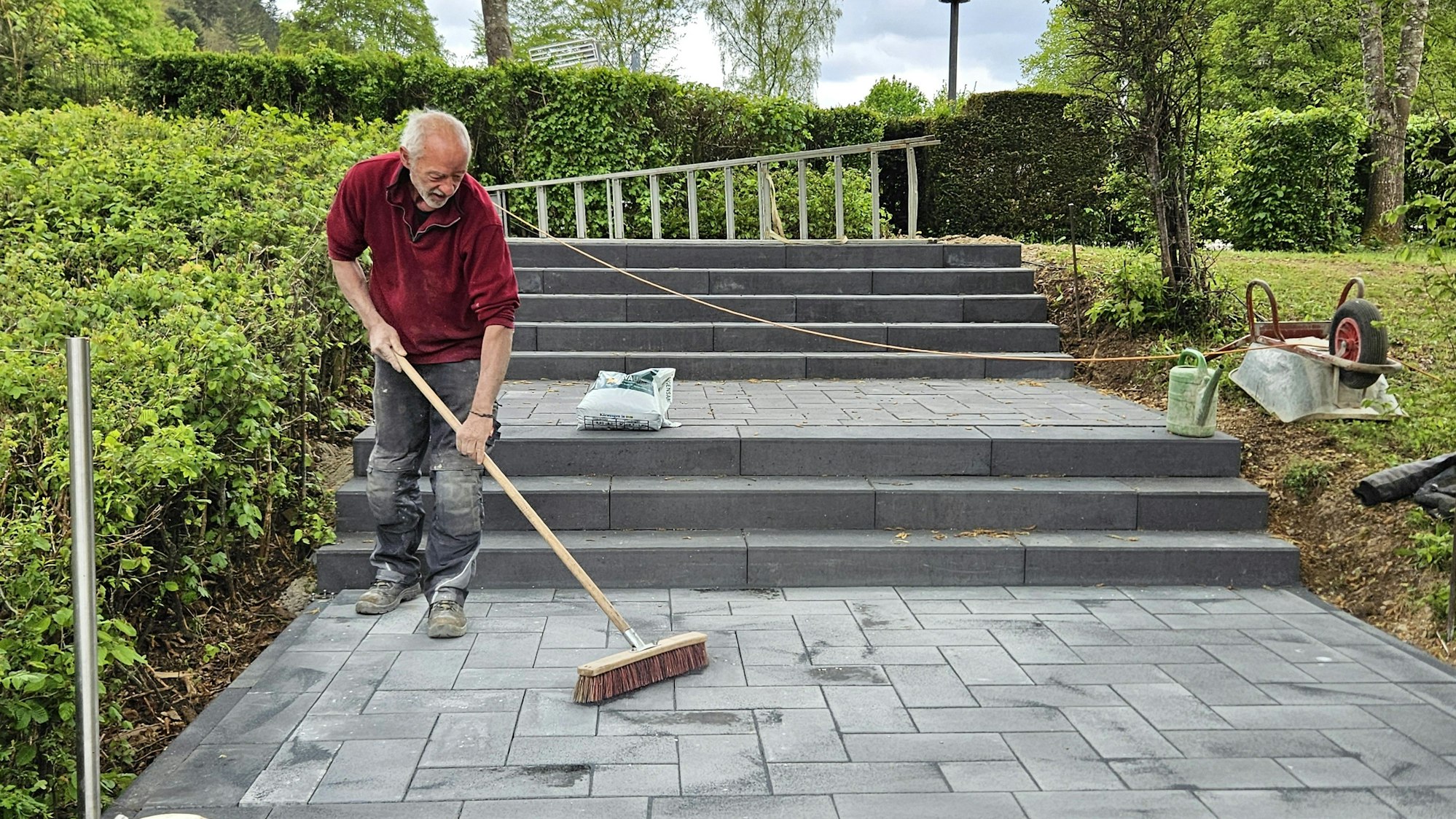 Ein Arbeiter verteilt den Fugensand zwischen den Platten der neuen Treppe.