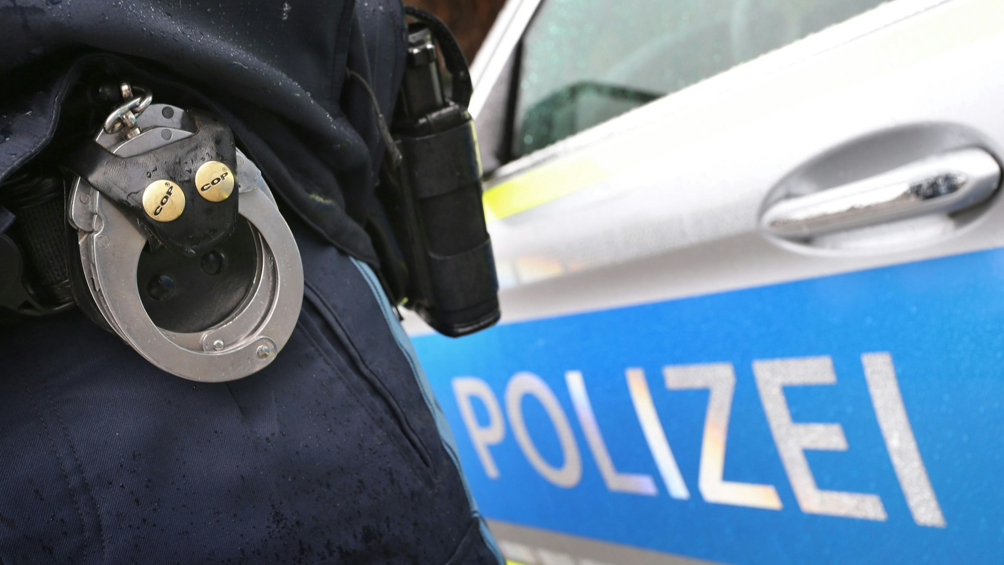 ARCHIV - 15.03.2019, Bayern, Kempten: ILLUSTRATION - Ein Polizist mit Handschellen und einer Pistole am Gürtel steht vor einem Streifenwagen. (zu dpa: «Abschiebehäftling nach Flucht wieder festgenommen») Foto: Karl-Josef Hildenbrand/dpa +++ dpa-Bildfunk +++