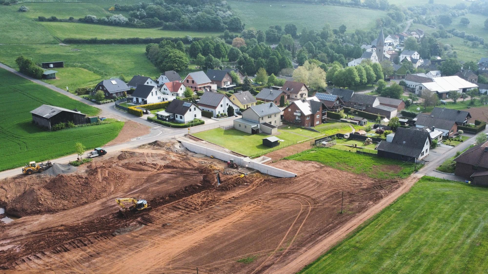 Die Drohnenaufnahme zeigt die Baustelle eines Regenrückhaltebeckens und im Hintergrund den Ort Kallmuth.