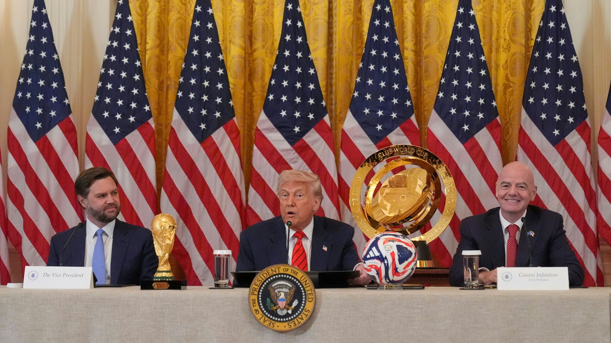 06.05.2025, USA, Washington: US-Präsident Donald Trump (M) spricht während einer Sitzung der FIFA-Task Force im East Room des Weißen Hauses während US_Vizepräsident JD Vance und FIFA-Präsident Gianni Infantino (r) zuhören. Foto: Mark Schiefelbein/AP/dpa +++ dpa-Bildfunk +++