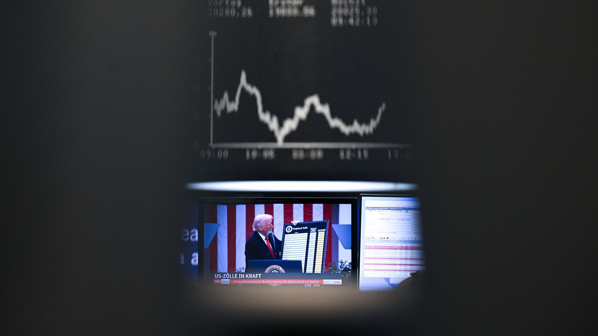 US-Präsident Trump ist auf einem Bildschirm auf dem Parkett der Frankfurter Wertpapierbörse vor der Anzeigetafel mit der Dax-Kurve zu sehen.