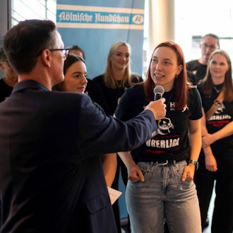 Lokalsportchef Thomas Schmitz interviewt Lea Schmitz bei der Sportlerwahl 2024. Die Mannschaft steht im Hintergrund.