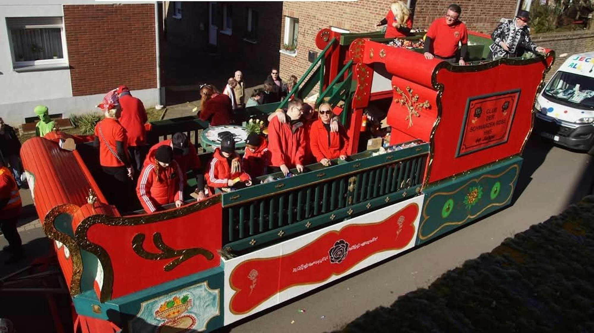 Zu sehen ist ein roter Karnevalswagen, auf dem Menschen stehen.