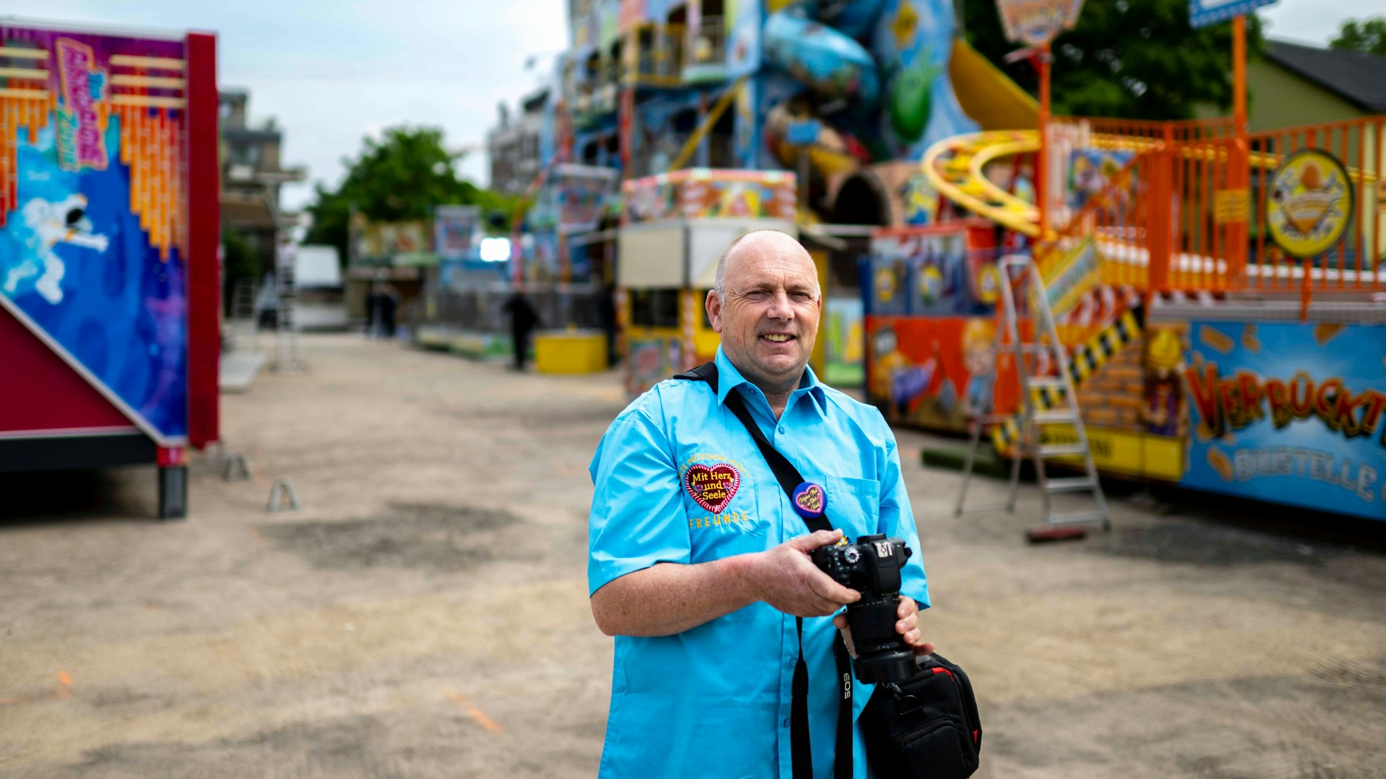 Helmut Pütz trägt ein hellblaues Hemd und hat eine Kamera in der Hand. Er geht vor der Eröffnung über den Kirmesplatz in Euskirchen.