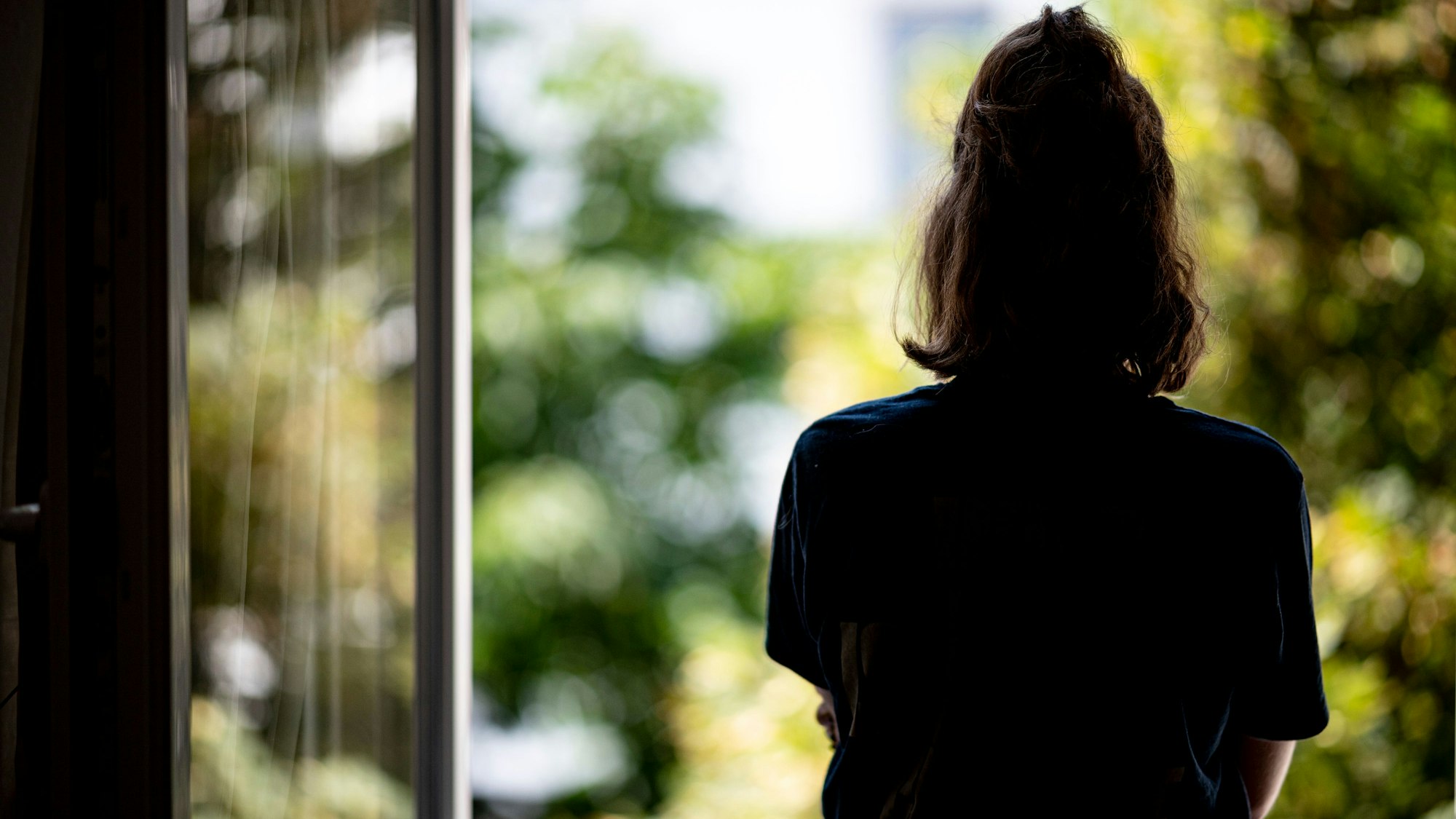 Frau steht an einem offenen Fenster (Symbolbild)
