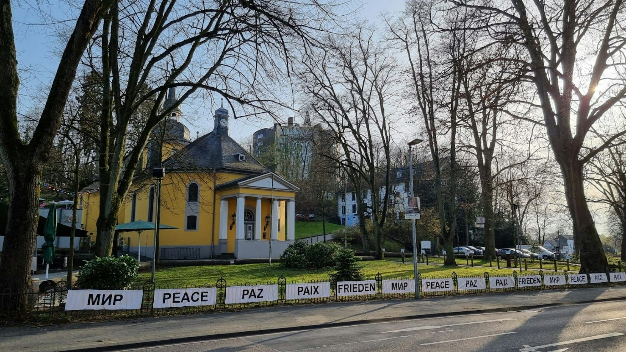 Eine Kirche mit gelber Fassade und Säulen vor dem Eingang. Davor Spruchbänder für den Frieden.