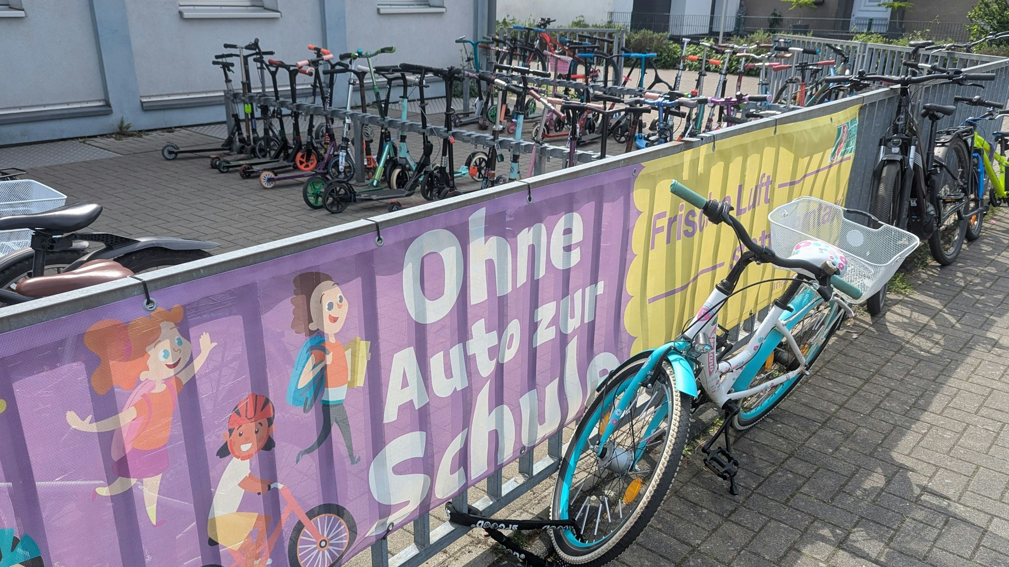 Das Foto zeigt große Spruchbanner am Zaun vor dem Fahrrad- und Rollerabstellplatz.
