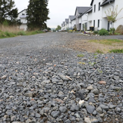 Eine Schotterstraße, im Hintergrund einige Häuser.