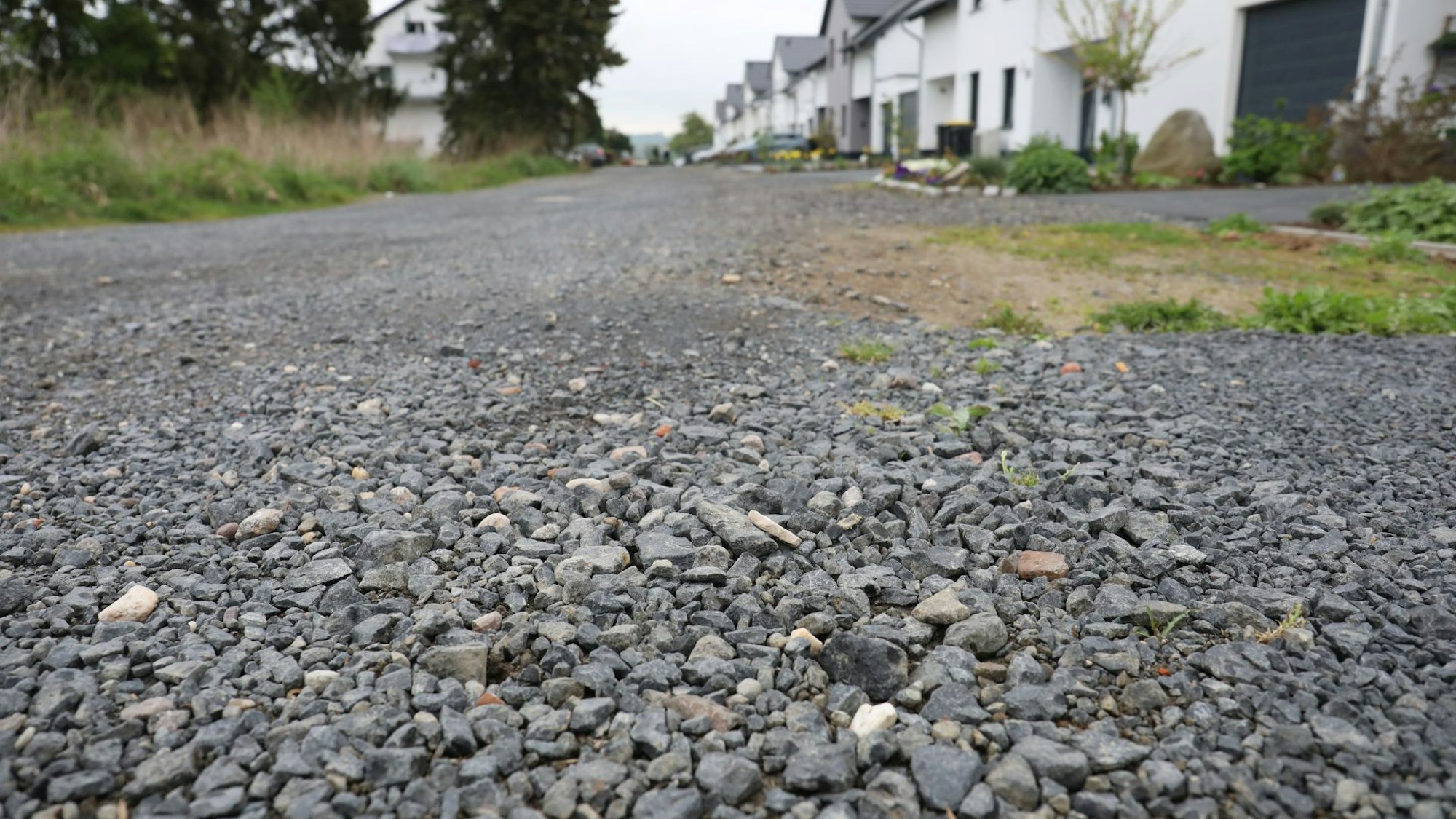 Eine Schotterstraße, im Hintergrund einige Häuser.