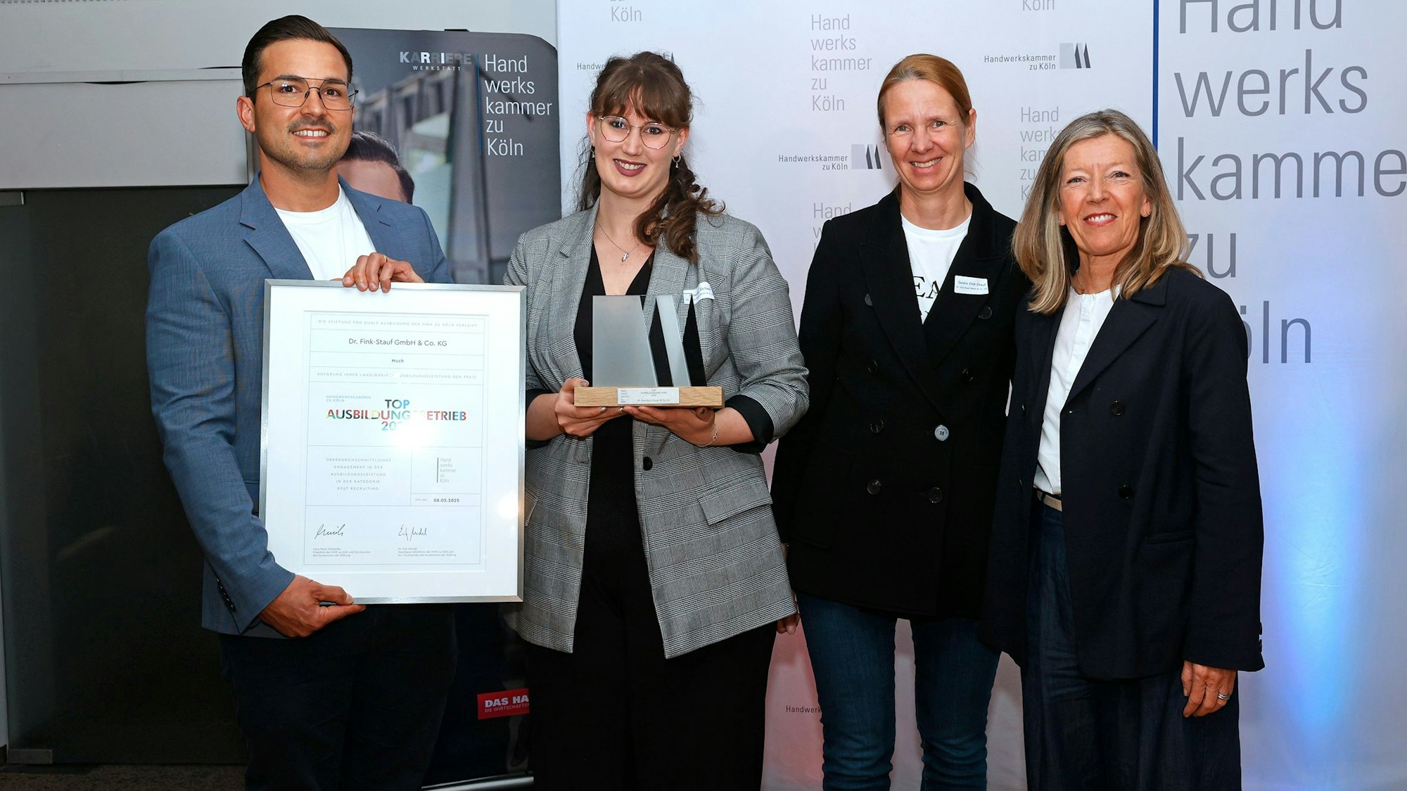 Vier Personen lächeln in die Kamera, ein Mann ganz links im Bild hält eine gerahmte Urkunde in die Kamera, eine Frau rechts neben ihm hält den Preis im Dom-Motiv.