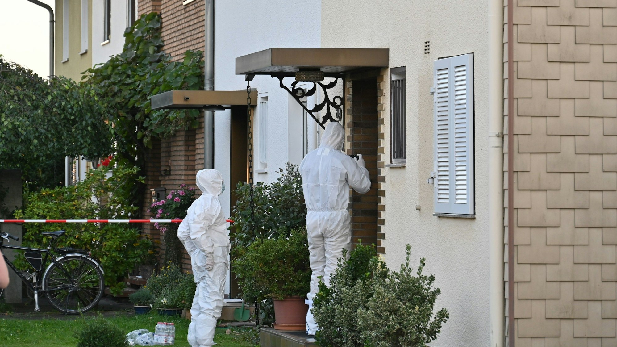 Das Bild zeigt Polizeibeamte in Schutzanzügen vor einem Haus.