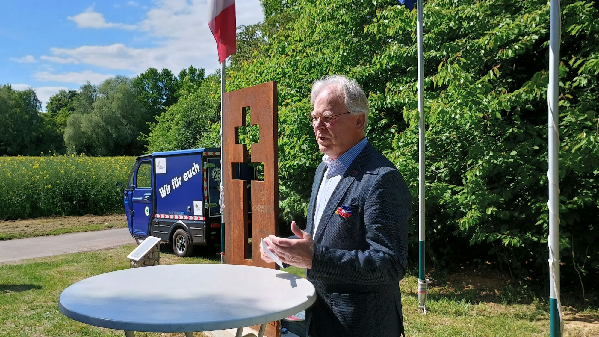 Hübner steht schräg vor dem Lothringer Kreuz. Das Kreuz hat zwei Querbalken und ist als Lücke in einer rostigen Stahlplatte sichtbar.
