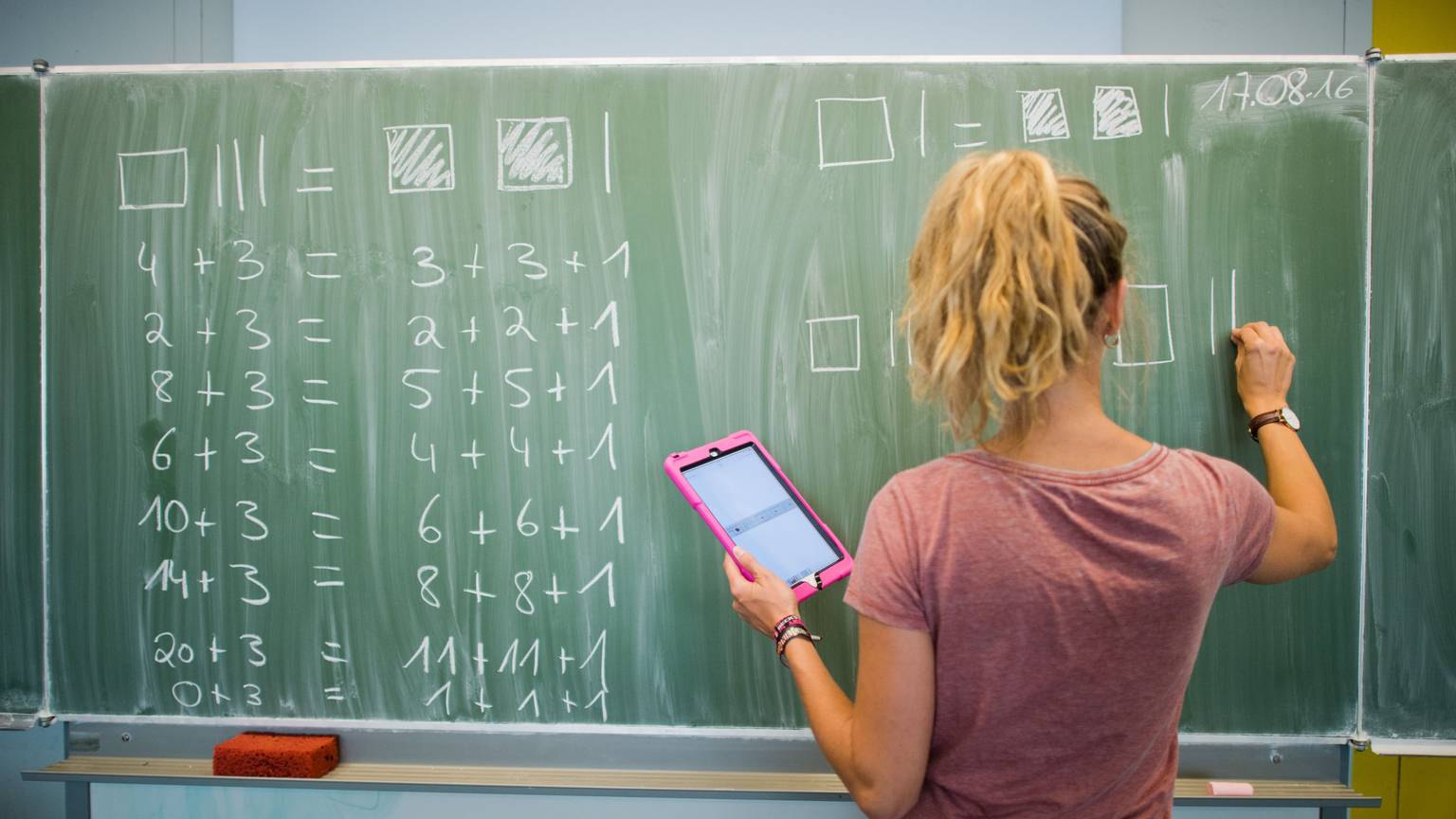 Eine junge Lehrerin schreibt an eine Schultafel im Mathematikunterricht einer 8. Klasse.