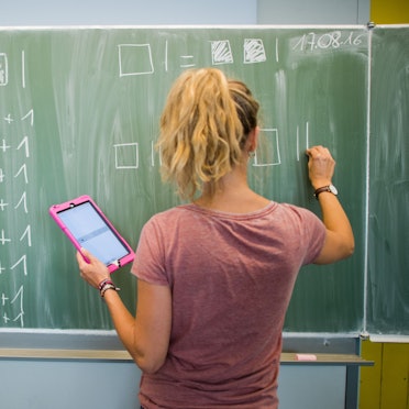 Eine junge Lehrerin schreibt an eine Schultafel im Mathematikunterricht einer 8. Klasse.