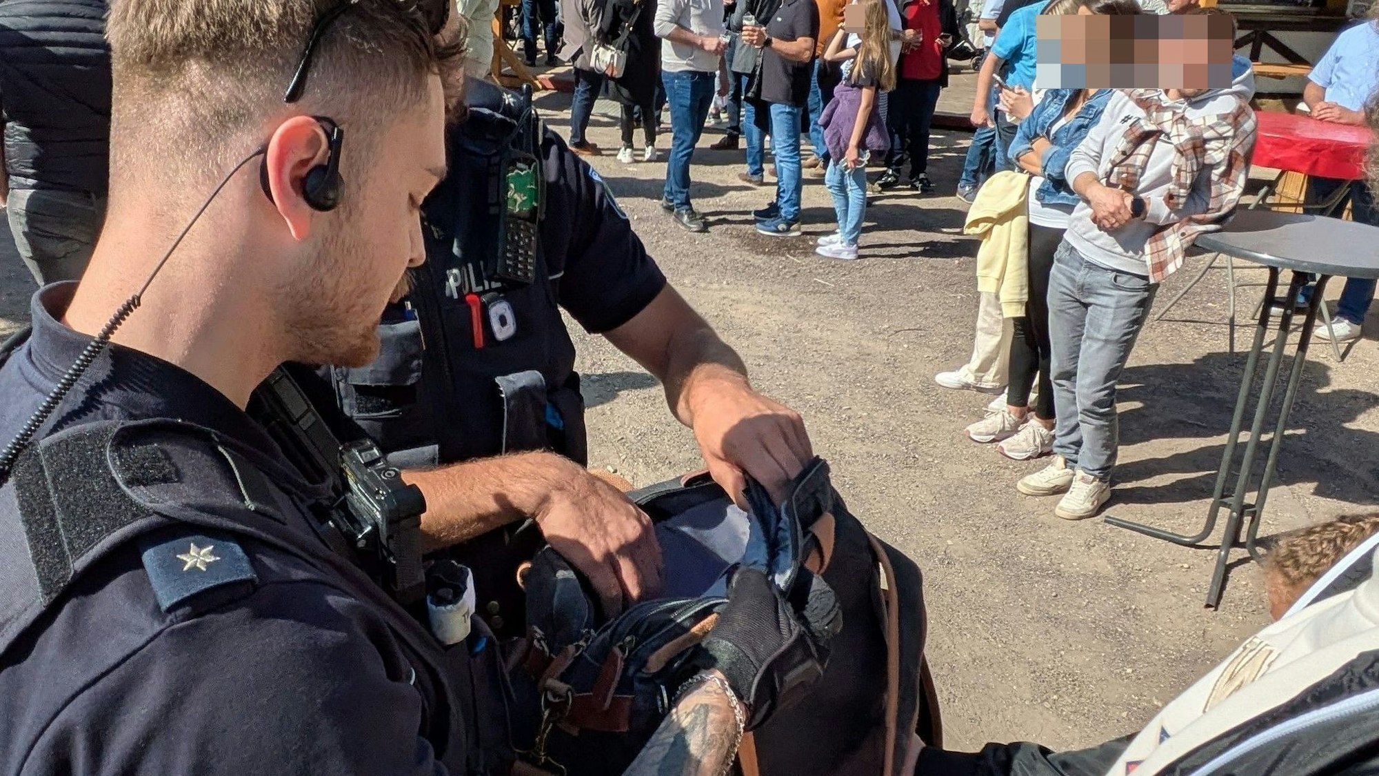 Zwei Polizisten führen auf der Kirmes in Euskirchen Kontrollen durch. Sie schauen in eine Handtasche.