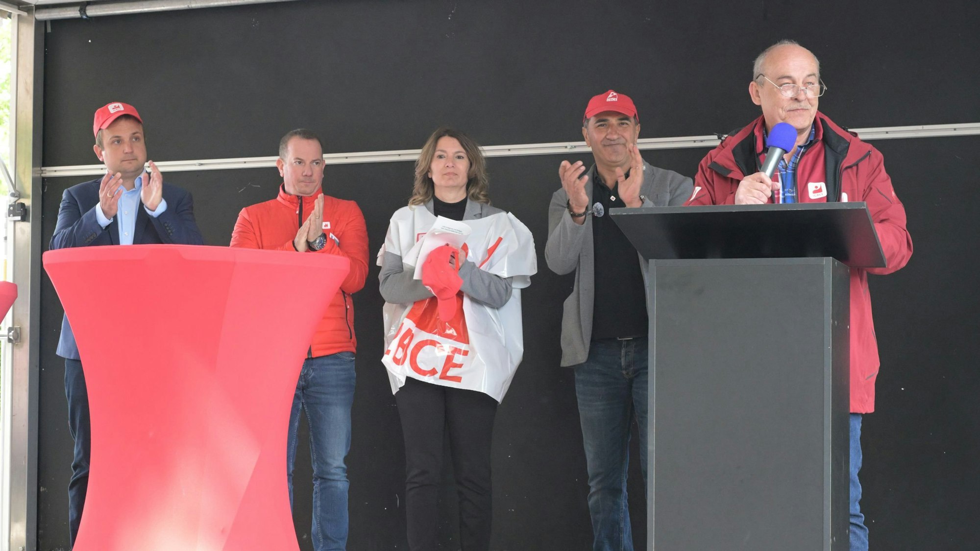 GBCE-Gewerkschaftssekretär Thomas John Dyer, Iman Özmen, MdL Tülay Durdu (SPD), IGBCE-Bezirksleiter Armando Dente und MdL Martin Lucke (CDU) stehen auf einer Bühne und sprechen beziehungsweise klatschen.
