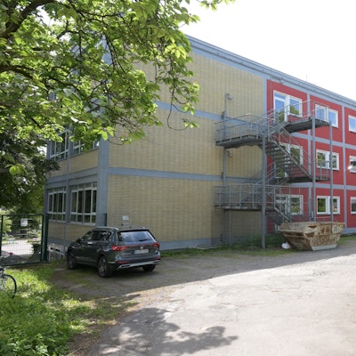 zwischen Bäumen und parkenden Autos ist die Gemeinschaftsgrundschule Bergisch Gladbach-Gronau zu sehen.